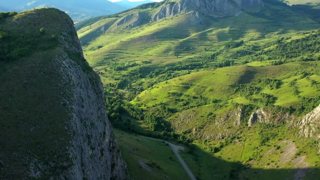 A tracking drone shot of the Apuseni mountain range, in Coltesti, Transylvania, Romania. The vast green mountains and valleys stretch into the distance on a sunny day.