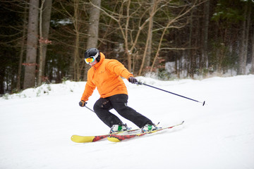 Fototapeta na wymiar Adult man skiing and bending on side for doing turning. Dark view of forest along the mountain slope on background. Concept of healthy lifestyle and active winter outdoors pastime in wild nature area