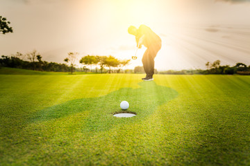 Silhouette golfer professional teeing golf ball to hole to winner in game at golf course with...