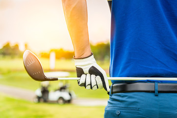 Close up hand of golfer holding golf club to preparing competition , he wearing blue shirt ,white and black golf glove with blur golf course background. - Powered by Adobe