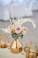 Wedding decoration in boho style. Light colors, in the tent. Wedding table decorated with gold vases with roses and cereals. And geometric candles in gold candlesticks.