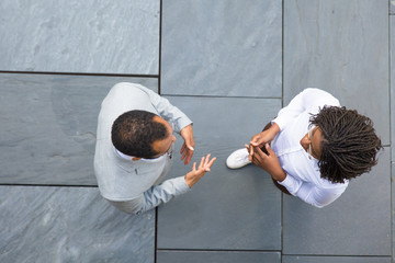 Business colleagues meeting near office and discussing project. Top view of business man and woman standing outside, talking and gesturing. Business conversation concept