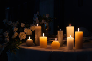 White rose and burning candles on a table in the dark, decoration of a festive table for dinner, space for text.