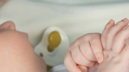 The little hand of a newborn baby of two months holds the fingers of his mother