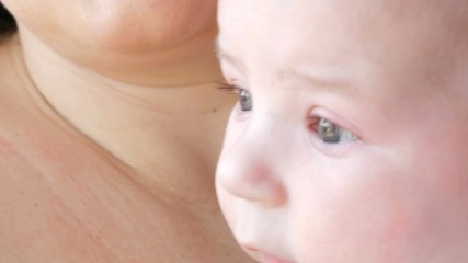 A two-month newborn baby lies on the mother arms and looks around