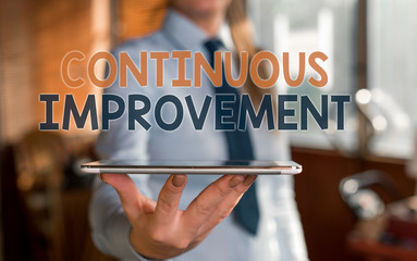 Writing note showing Continuous Improvement. Business concept for ongoing effort to improve products or processes Blurred woman in the background pointing with finger in empty space