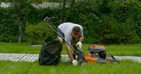 gardener is cleaning lawnmower in yard of house in summer day