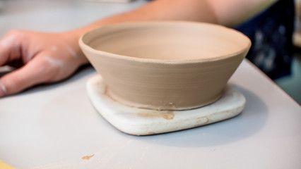 A raw clay pot in the hands of a potter. Workshop in the pottery workshop. Clay pot on a potter`s wheel