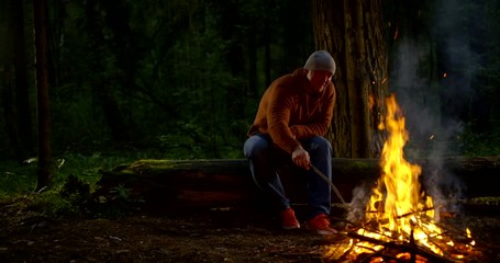 alone male tourist is resting in forest near campfire at night time looking on flame