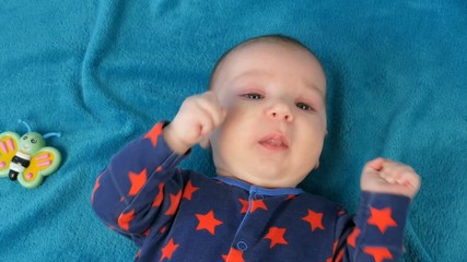 Portrait of beautiful funny little newborn baby of two months lying on blue bedspread surrounded by baby rattles