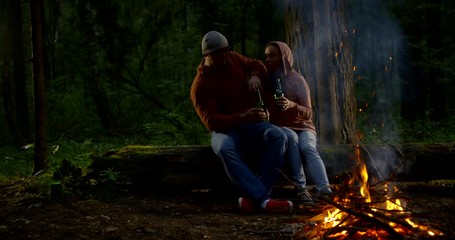 romantic loving pair is sitting near campfire on lawn of forest in nighttime