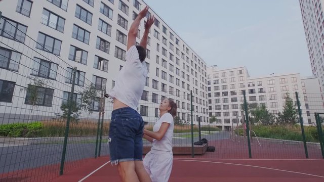 Excited couple runs for basketball, follow the ball. Girl takes leadership, controls, dribbler, jump and throw in basket. Man try to hindrance. Slow motion.
