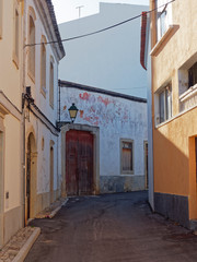 Fototapeta na wymiar A narrow side street during Siesta in the small Portuguese town of Estoi in the Algarve, with an ornate street lamp attached to the walls of the houses. Portugal.