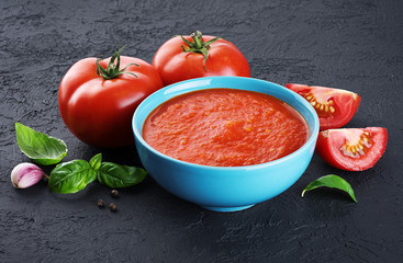 Bowl of tomato soup, tomatoes, garlic and basil on a dark background.
