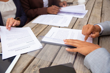 Business people studying contract terms at meeting. Business man and women sitting at cafe table and reading documents. Paperwork closeup concept
