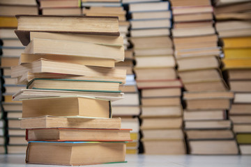 A stack of old books in hard binding against the shelves of books in the library. A stack of books 