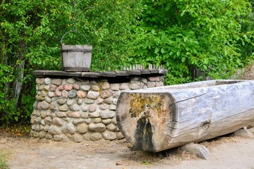 Rural landscape. Old well made of stones, old wooden bucket and a bowl for water made of a log of wood. Village tradition, Poland