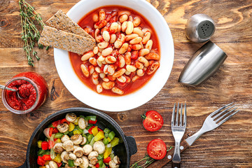 Tasty beans with tomato sauce and vegetables on wooden table
