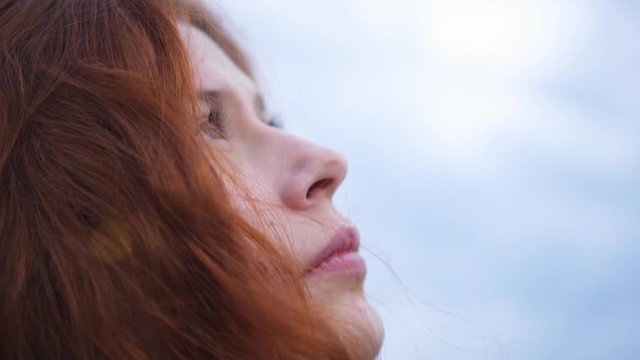 Сlose up Portrait of Beautiful Redhead Woman Exploring Spirituality Looking up Praying with Wind Blowing Hair Lens Flare