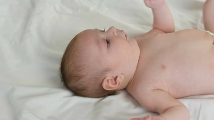 Portrait of beautiful funny little newborn baby of two months lying on white bed. Mom dresses the baby