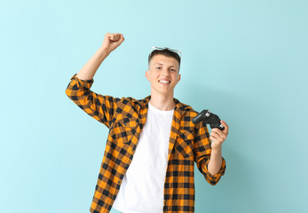 Happy teenage boy playing video game on color background