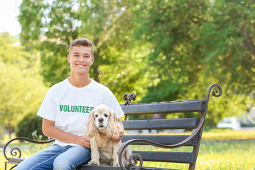 Teenage volunteer with cute dog sitting on bench outdoors