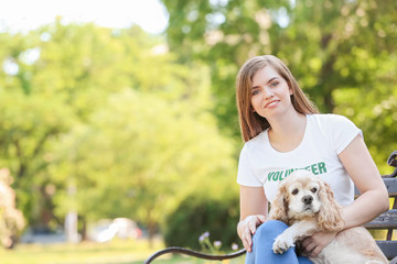 Female volunteer with cute dog sitting on bench outdoors