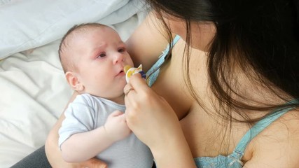 A two-month newborn baby lies on the mother arms and sucks the nipple. Mother tries to put her child to sleep
