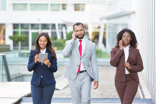 Diverse business colleagues with gadgets going along urban glass facade. Business man and women walking outside, using tablet, talking on phone. Team and digital technology concept