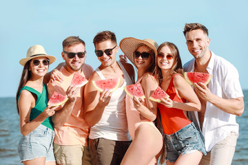 Happy friends eating watermelon on sea beach at resort