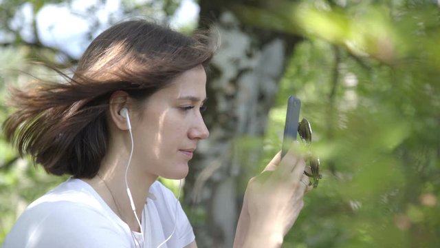 Portrait of Young woman listens to music with phone and headphones enjoying sound park forest background. Young woman resting in park or forest