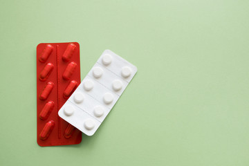 Medicine capsules and tablets  in red and white blister packs on a green background. Isolated. Copy space.
