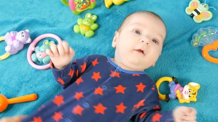 Portrait of beautiful funny little newborn baby of two months lying on blue bedspread surrounded by baby rattles