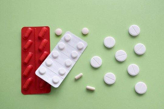 Medicine capsules and tablets  in red and white blister packs on a green background. Isolated. Copy space.