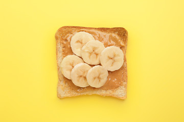 Tasty toasted bread with banana and peanut butter on color background