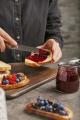 Woman spreading tasty berry jam onto toasted bread, closeup