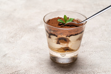 Portion of Classic tiramisu dessert in a glass cup on concrete background