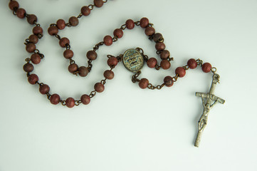 Closeup Jesus Christ crucifix and rosary with brown beads isolated on white background.