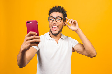 Great shoked news! Portrait of handsome excited cheerful amazed delightful curious guy wearing casual sending and getting messages isolated against yellow background. Using phone.
