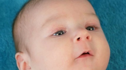 Portrait of beautiful funny little newborn baby of two months lying on blue bedspread surrounded by baby rattles