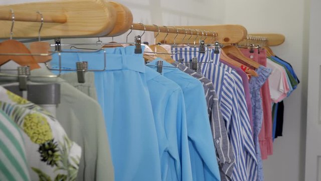 camera motes along wooden hangers with fashionable colorful summer clothes on rack in modern designer shop close view
