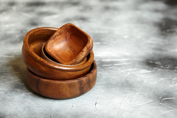 Stack of empty wooden bowls on grey background with copy space. Many round and square salad bowls on stone table with black paint stains, side view. Pile of kitchenware from natural material