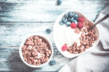 Greek yogurt, blueberries, raspberries and granola in a white bowl on a wooden background