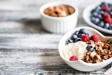 Greek yogurt, blueberries, raspberries and granola in a white bowl on a wooden background