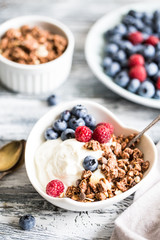 Greek yogurt, blueberries, raspberries and granola in a white bowl on a wooden background