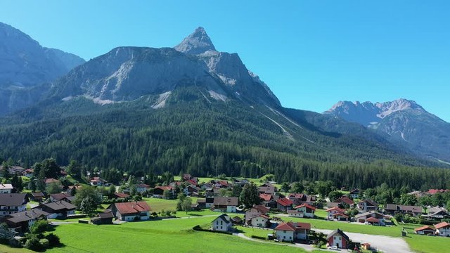 Aerial view of Tyrolean village Ehrwald surrounded by mountains during summer, lush green hills and clear blue sky - landscape panorama of Alps from above, Germany/Austria border, Europe
