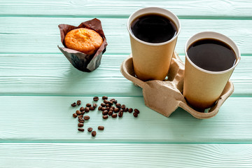 paper cups with black coffee and cappuccino to take away, beans, muffin on mint green wooden background