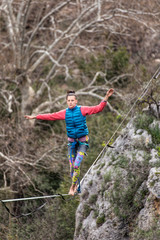 Fototapeta premium A woman is walking along a stretched sling. Highline in the mountains. Woman catches balance. Performance of a tightrope walker in nature. Highliner on the background of valley.