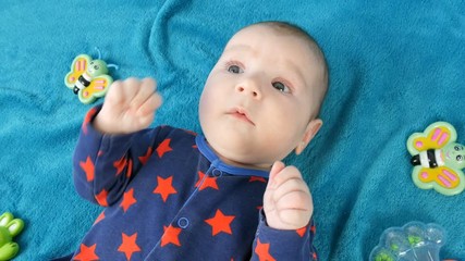 Portrait of beautiful funny little newborn baby of two months lying on blue bedspread surrounded by baby rattles