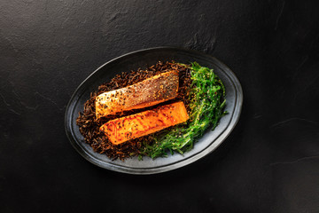 Roasted salmon with sesame seeds, wakame seaweed and wild rice on a black background